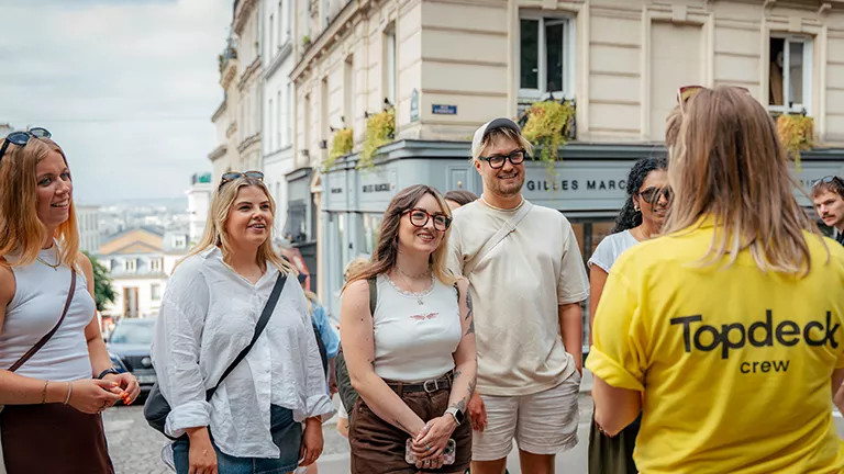 A trip leader wearing a Topdeck uniform talks to a group of people on a quiet street in Paris.