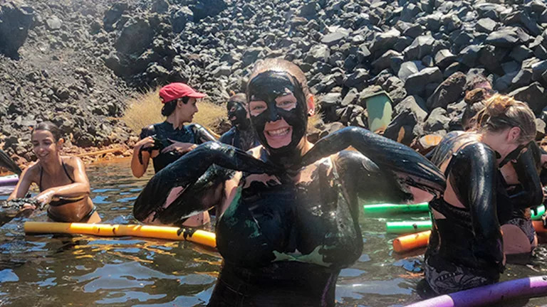 Person wearing a swimsuit covered in black volanic mud.