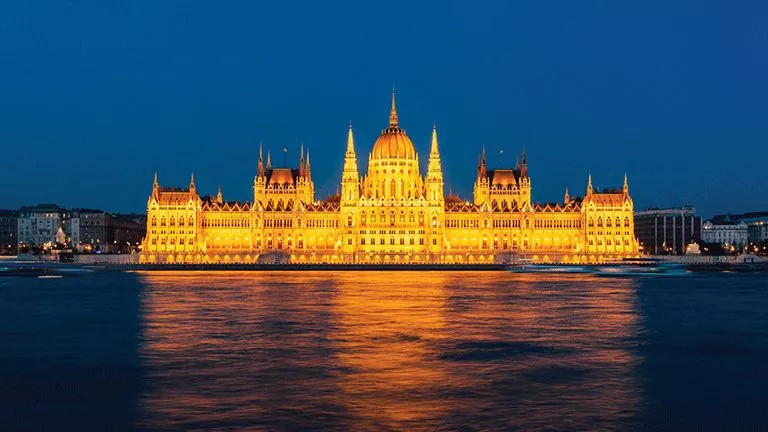 The long Hungarian Parliament building illuminated at night along the Danube River.