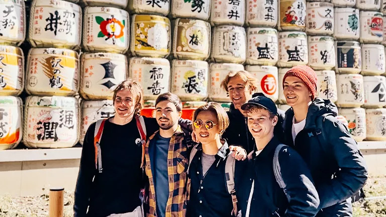 Group of people pose together in front of Japanese sake barrels at a Shinto shrine.