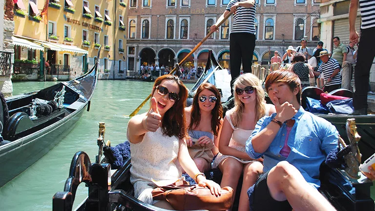 People taking a gondola boat ride in Venice. One person holds up their thumb in a positive gesture.