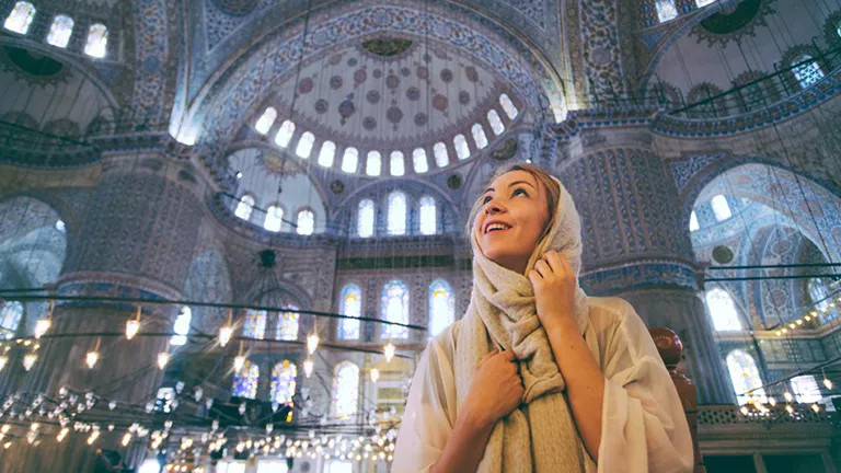 Person wearing a scarf looks up at the detailed ceiling of the Blue Mosque in Istanbul.