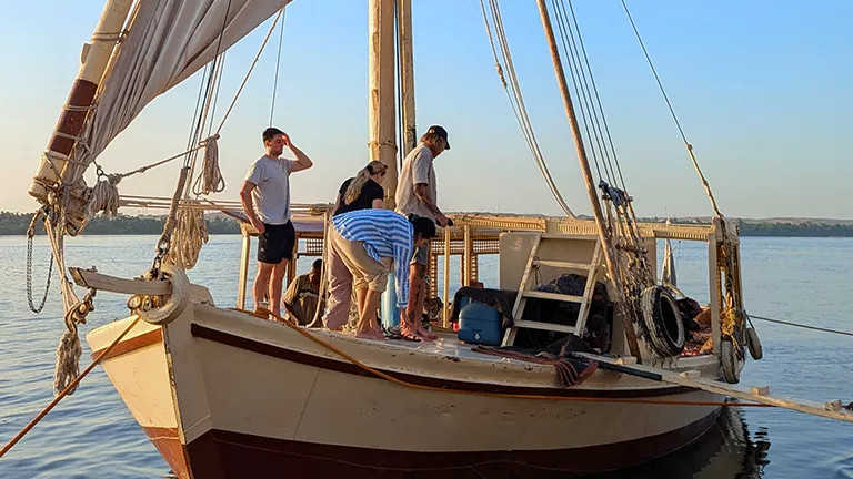 People standing on the bow of a traditional felucca boat.