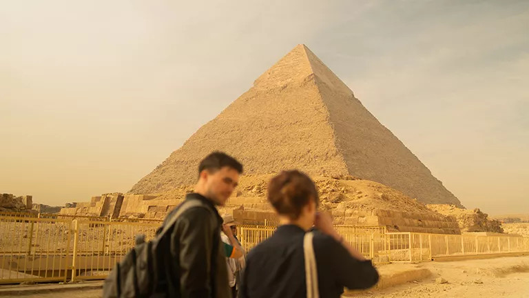 Two people walking and talking with an Egyptian pyramid ahead of them.