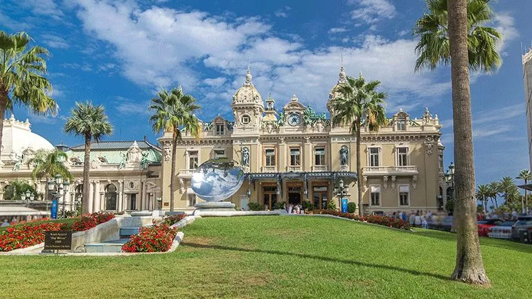 European stone coloured building surrounded by a lush garden and palm trees.
