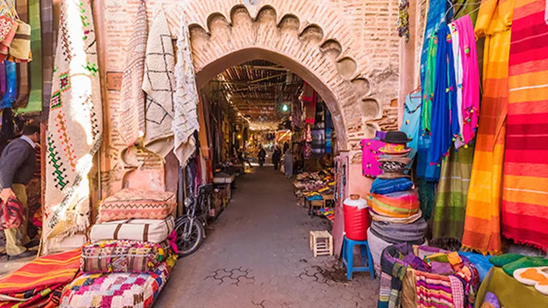 Archway of the Medina souks of Marrakech with bright coloured fabric hanging on each side.