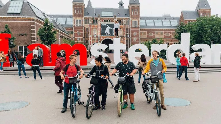 People standing with bikes in front of the large Amsterdam letters sign.