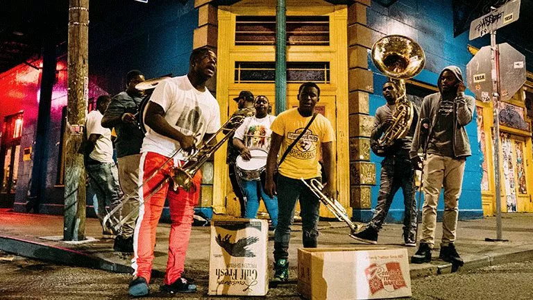 Street performers holding large trumpets and trombones at night.