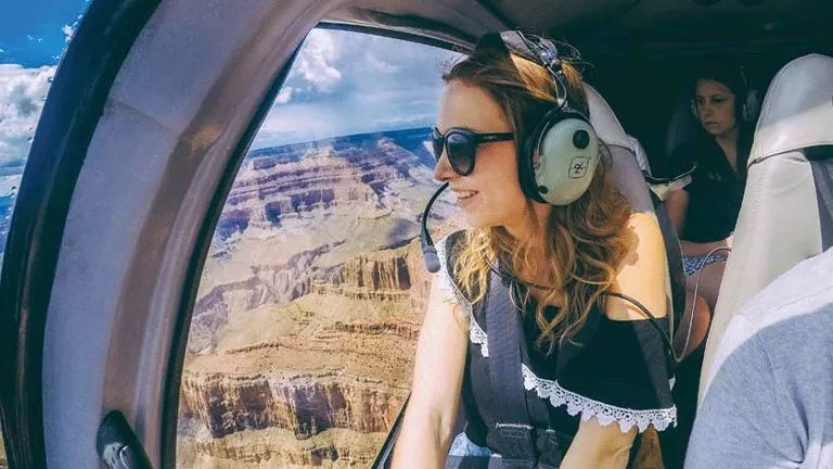 Person wearing headset while sitting in the cockpit of a helicopter flying over the Grand Canyon.