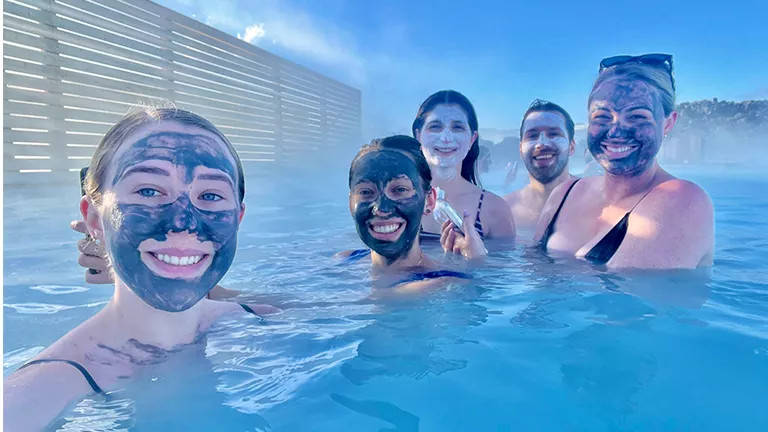 People with volcanic mud masks on their faces soak in a blue hot water lagoon.