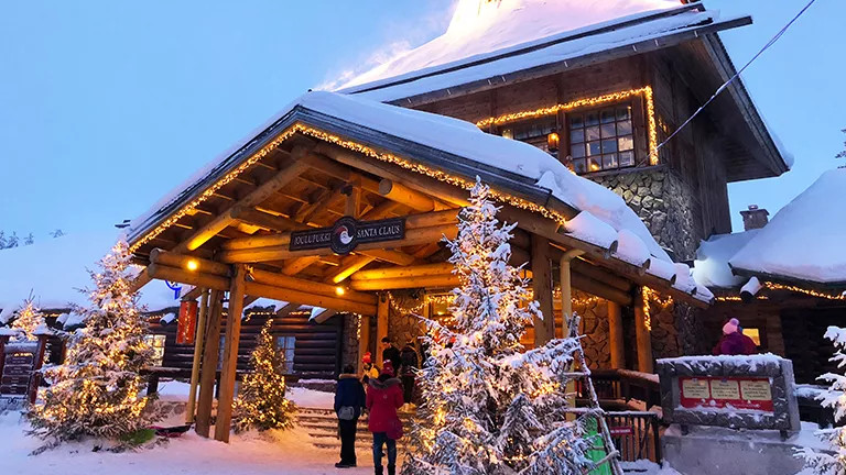 Snow covered wooden building with Christmas lights lining the entrance.