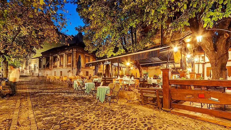 Cobblestone street in the evening with warm lights and tables ready to dine at.