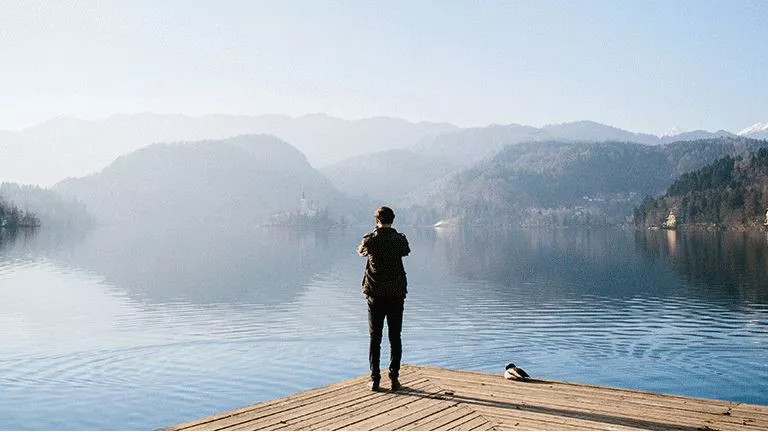 Person standing on the edge of Lake Bled while taking a photo.