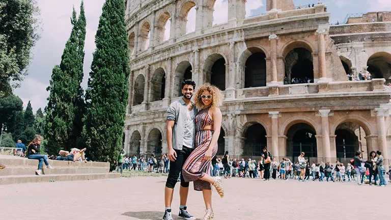 Two people posing in front of the colosseum in Rome.