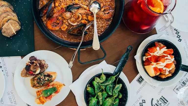 Table covered in Spanish tapas and paella with a jug of sangria.