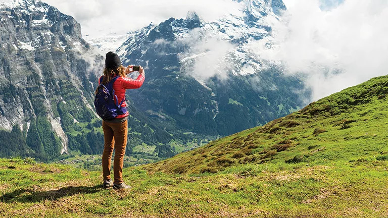Person taking a photo with a snowcapped mountain range in the background.