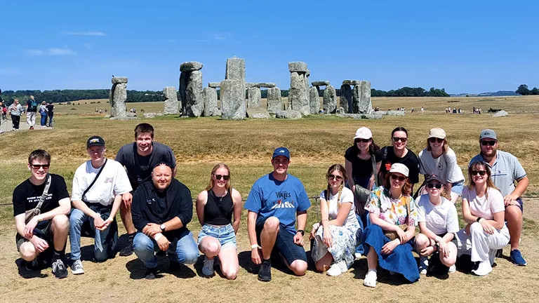 People crouching down and posing together for a photo in front of Stonehenge in the UK.