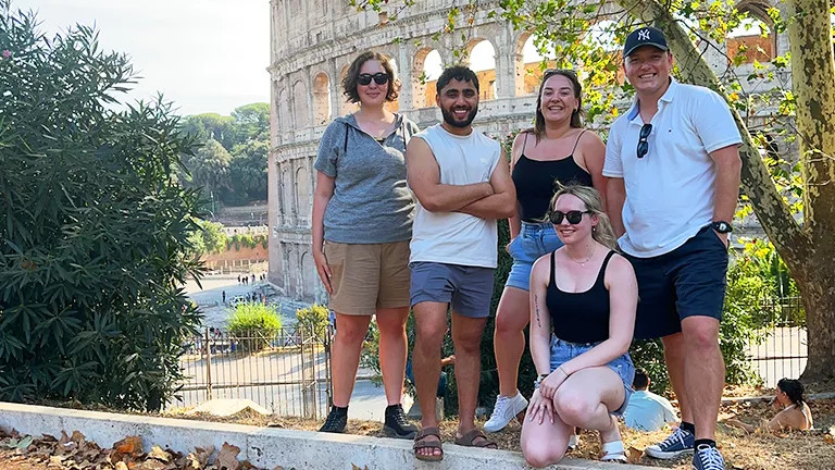 Five people posing for a photo in front of the Colosseum in Rome