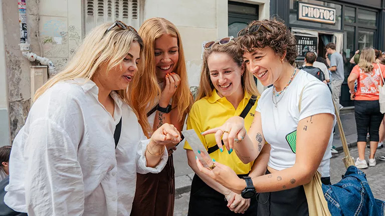 Group of people stand together looking at a photo strip printed from a photobooth in Paris.