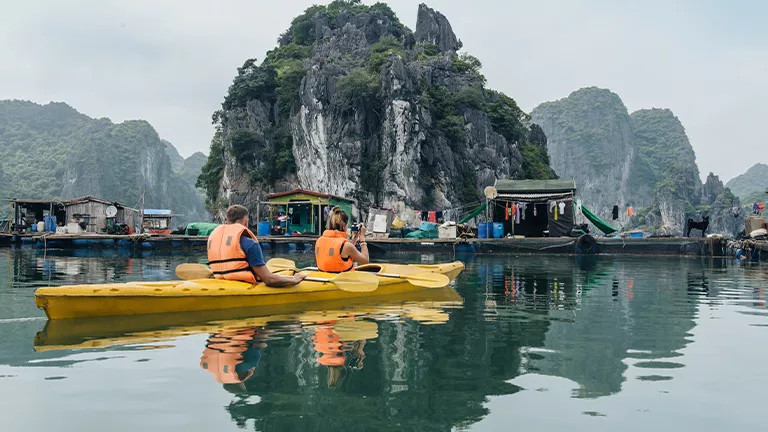 People kayaking in the green water of Ha Long Bay.