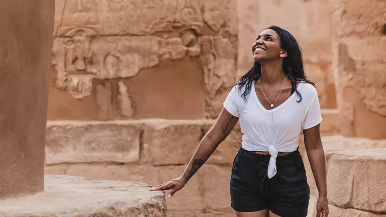 Person walking through Egyptian temple with hieroglyphs carved into the walls.
