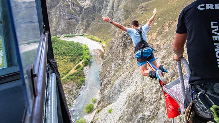 Person jumps of platform above a river with harness and bungy cord in Queenstown.