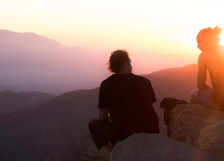 Three Topdeck travelers resting on some rock with the sun setting in the background.