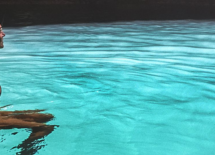 Topdeck traveler in a swimsuit sitting on a tied rope in a natural pool during a trip to Mexico.