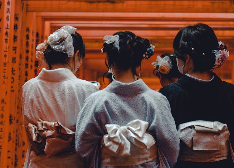 Three ladies in a kimono walking under Torii gates at the Fushimi Inari Shrine