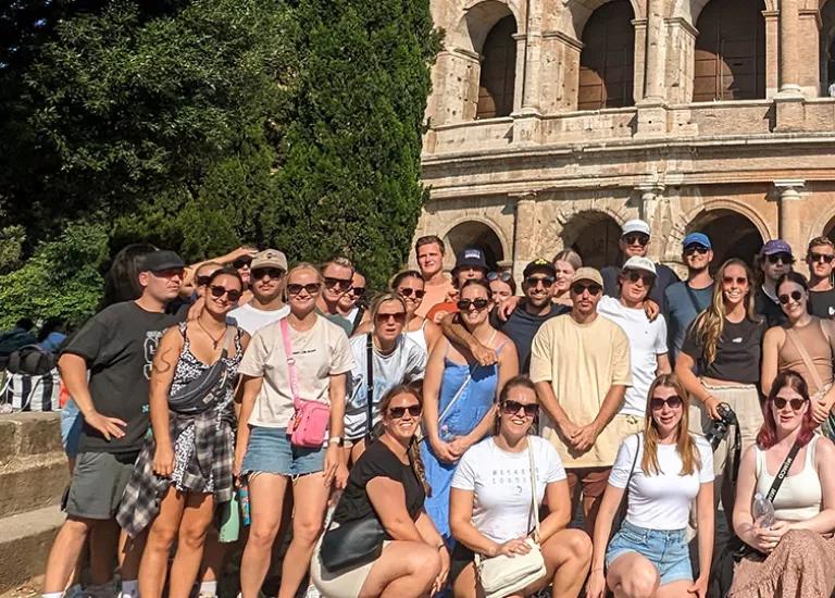 Topdeck travellers posing for a photo in front of the grand Colosseum of Rome