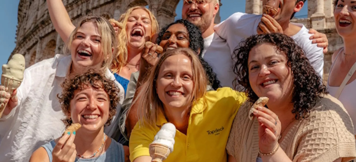 Group of people standing together in front of the colosseum in Rome while holding gelato and cannoli.