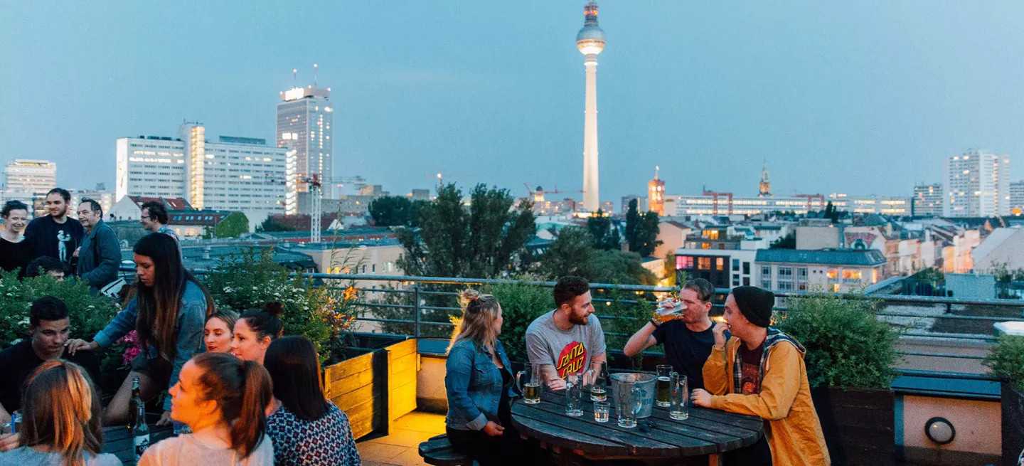  People drinking at a picnic style table at a rooftop bar in Berlin.