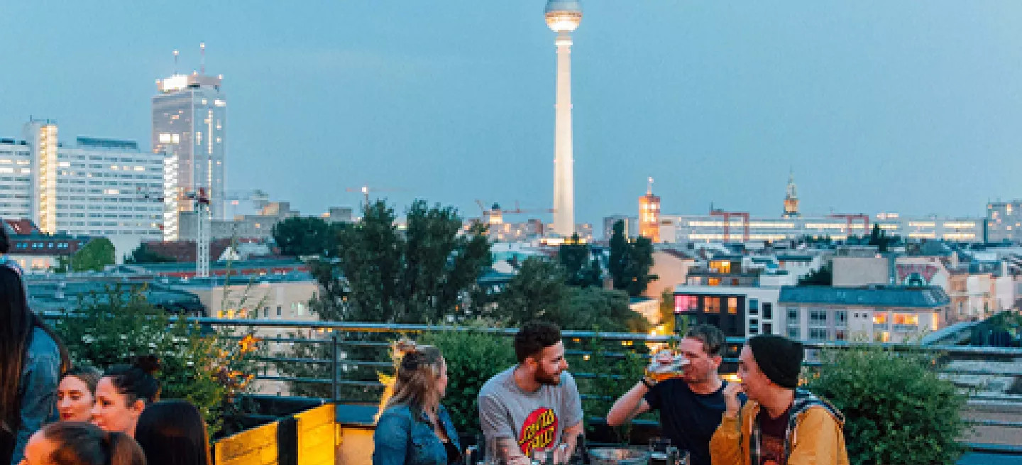  People drinking at a picnic style table at a rooftop bar in Berlin.