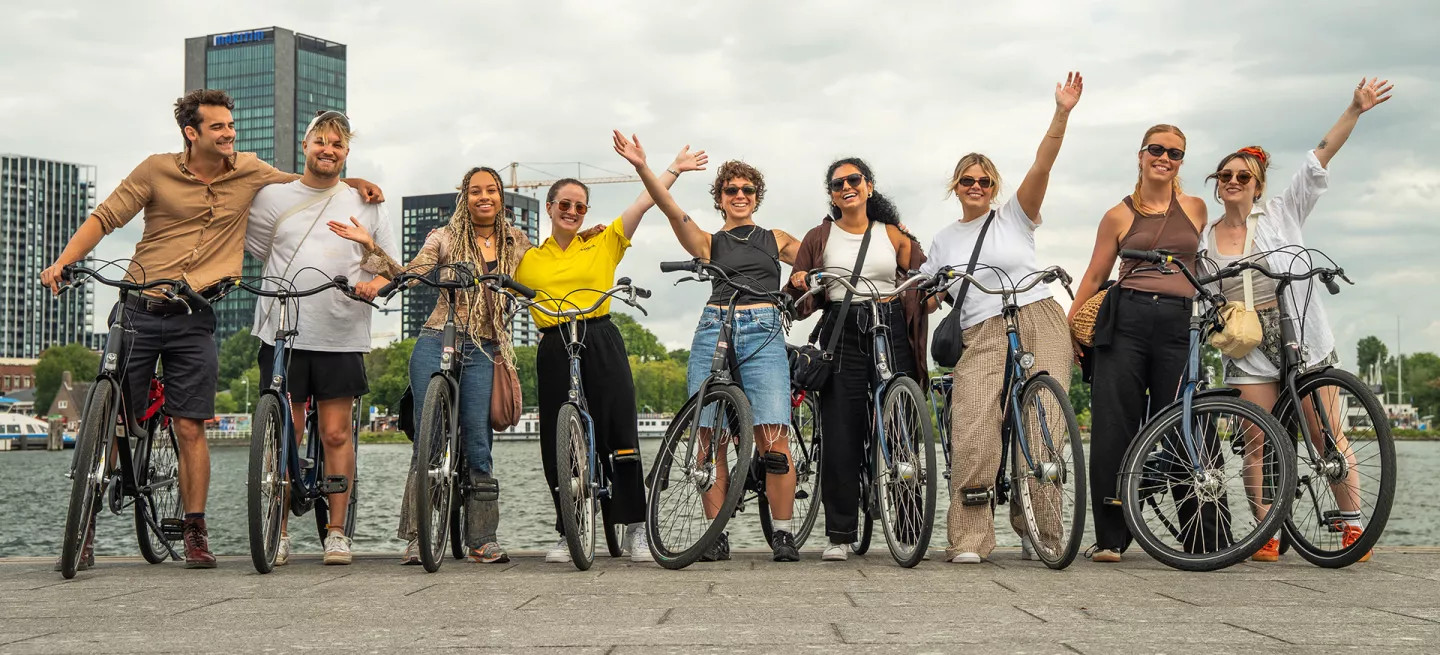 People standing together in a row with bikes near the river in Amsterdam.