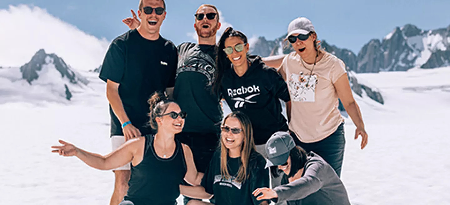 People posing together for a photo while standing on an snowy glacier in New Zealand.
