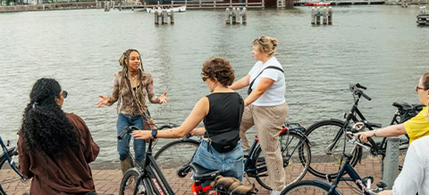 Group of people standing with bikes, listening to person speak by the river in Amsterdam.
