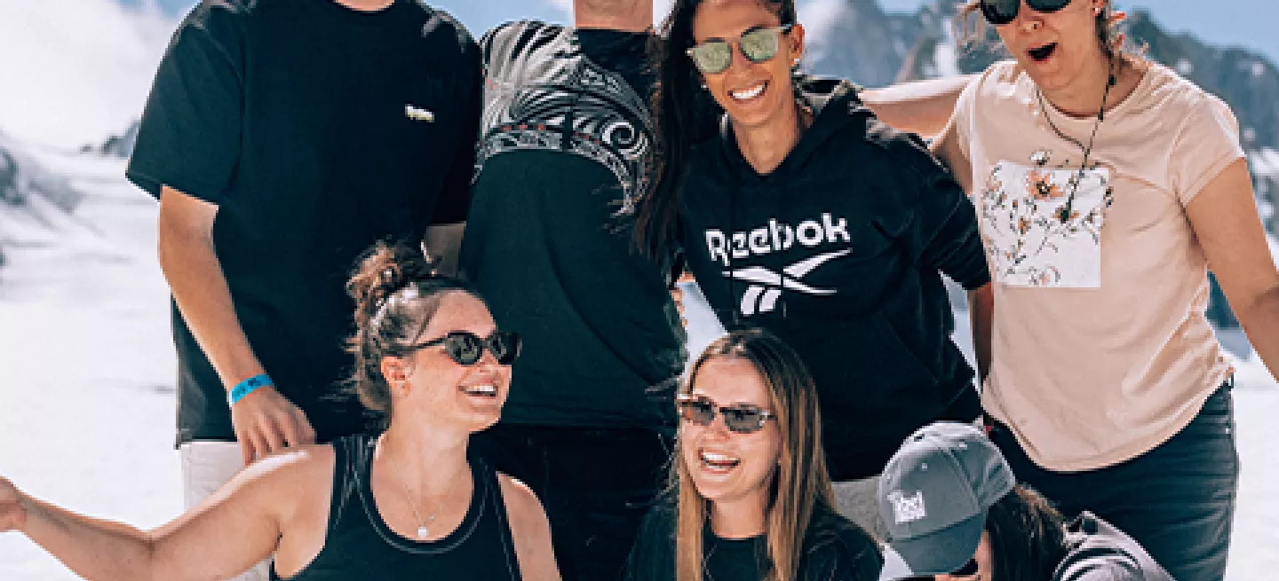 Group of seven people posing together smiling while standing on a the snow of a glacier in New Zealand.