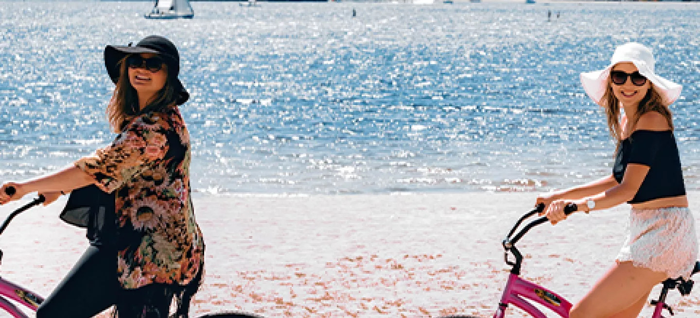 Three people riding bikes along the beach in San Diego with the sun sparkling on the water behind them.