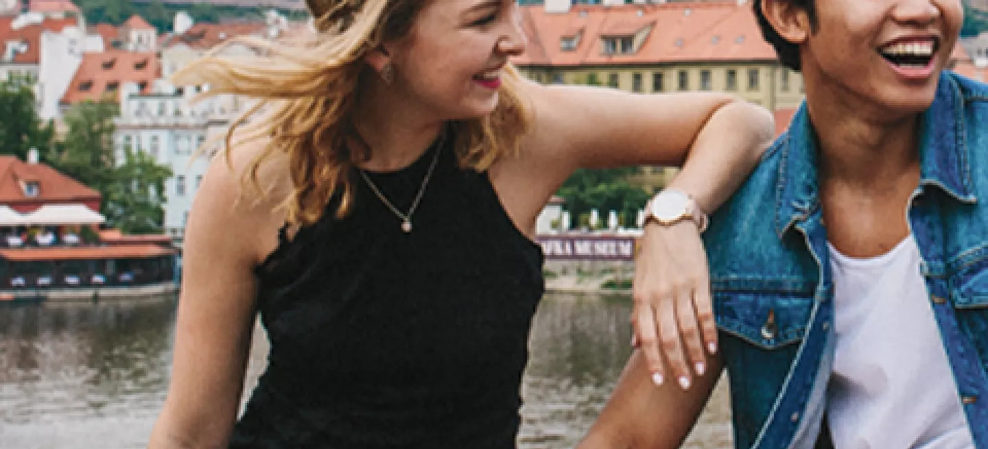 Three people sitting on a bridge in Prague with the river and a castle behind them.