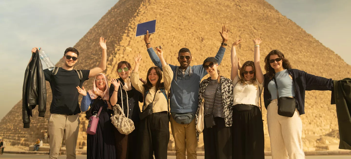 roup of people stand in front of a pyramid in Egypt with their hands in the hair.