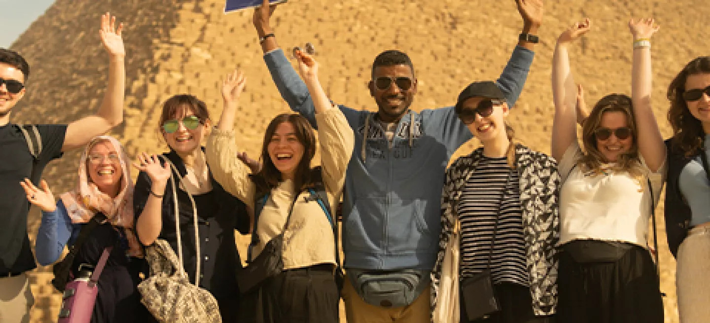 roup of people stand in front of a pyramid in Egypt with their hands in the hair.