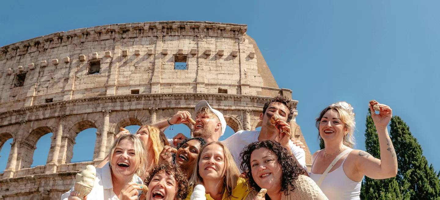 Group of people posing with ice cream and conoli in front of the Roman Colosseum.