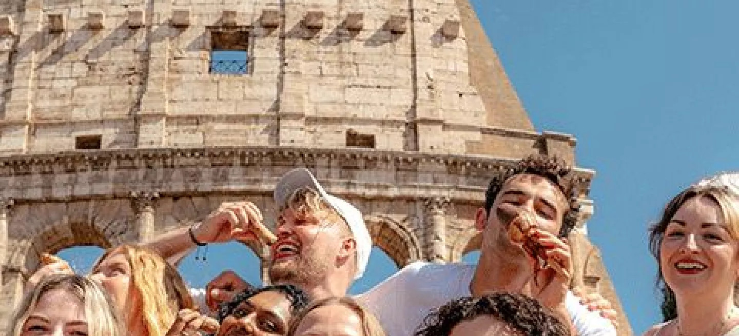 Group of people posing with ice cream and conoli in front of the Roman Colosseum.