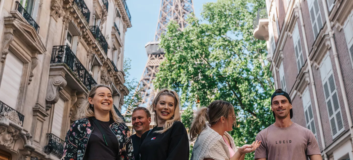 Group of people standing together smiling in different directions with the Eiffel Tower in the background above them.
