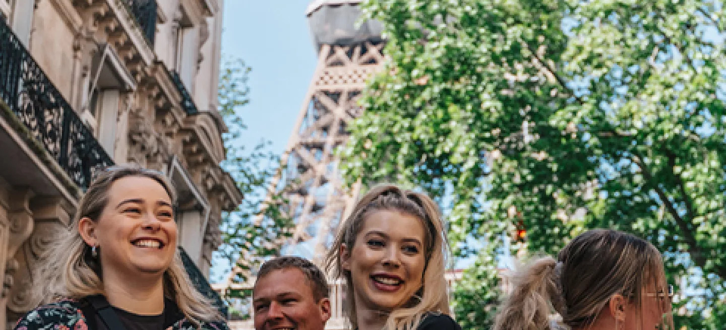 Group of people standing together smiling in different directions with the Eiffel Tower in the background above them.