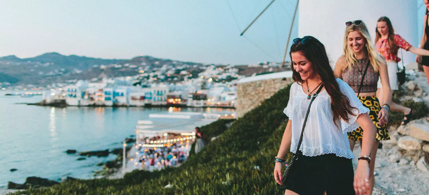 People walking down a slope near the Windmills of Mykonos in the evening.
