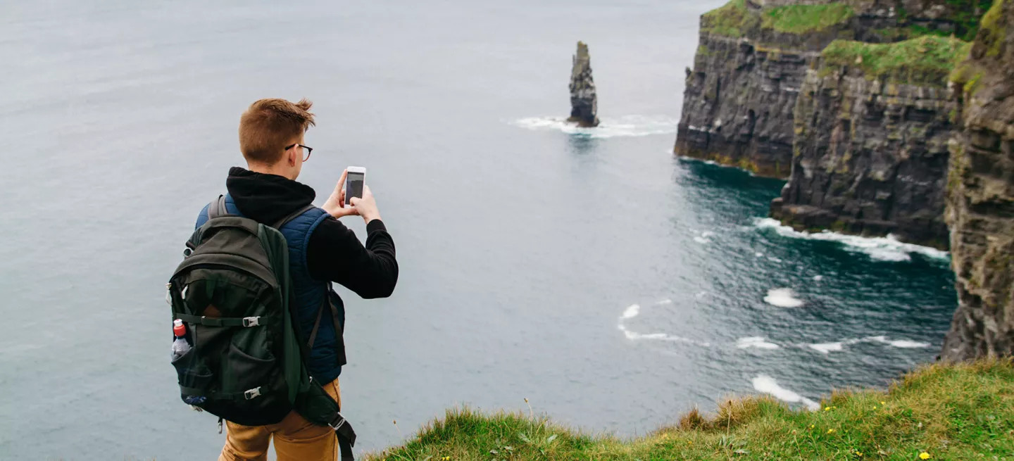 Person taking a photo on their phone of the Cliffs of Moher in Ireland.