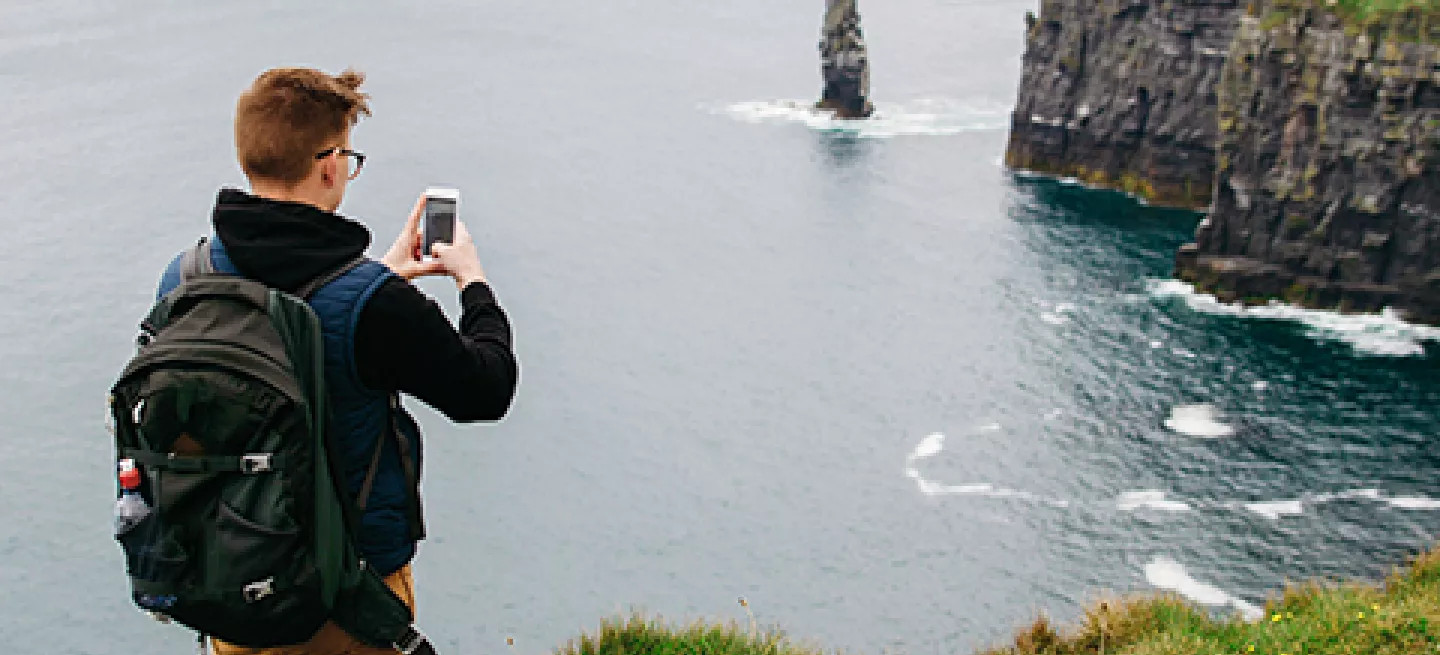 Person taking a photo on their phone of the Cliffs of Moher in Ireland.