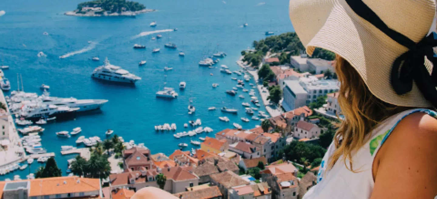 Person wearing a sunhat sitting and looking over a Croatian city and a harbour with many boats.