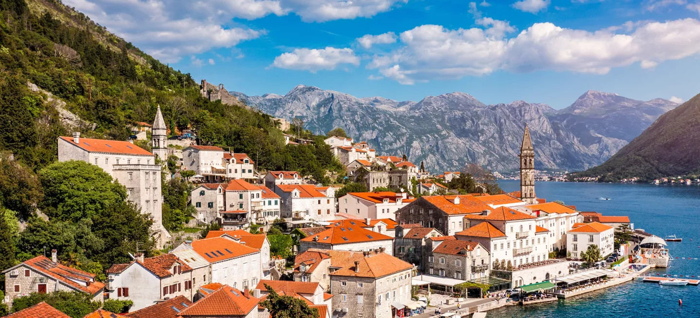 White buildings with orange rooves line the water in the town of Perast, located in the Bay of Kotor, Montenegro.